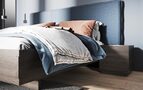 Bett aus dunklem Massivholz mit Kopfteil aus blauem Stoff